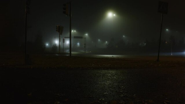 Truck passes the empty night crossroads. Night city in fog in winter. Reflection on wet asphalt