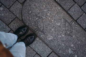Women's feet in black boots on the sidewalk. Seagulls are painted on the gray tile. The woman is...