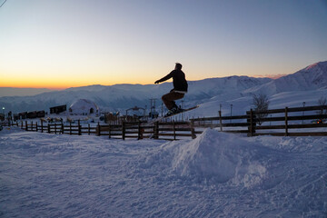 Silhouette of a man jumping mid-air while skiing down a slope in a beautiful sunset