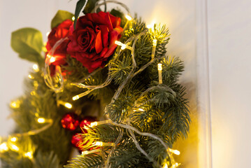 A New Year's wreath decorated with a garland and red roses hangs on the wall