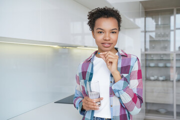 Mixed race young girl takes pills, vitamins, dietary supplement for wellness holding glass of water