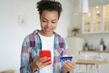 Happy mixed race teen girl holding bank credit card, shopping on smartphone. Online banking services