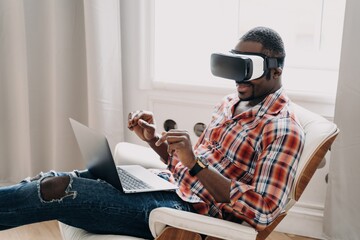 African american man in vr glasses working in cyberspace at laptop, interacting with virtual reality