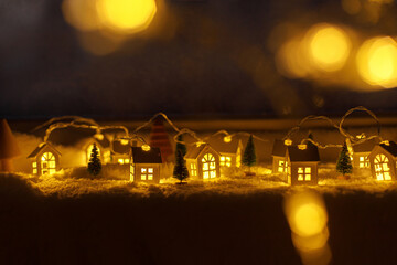 Cozy christmas miniature village. Stylish cute little glowing houses and christmas trees on soft snow blanket with lights bokeh in evening. Atmospheric winter village still life. Merry Christmas!