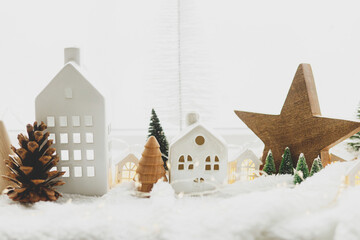 Cozy christmas miniature village. Stylish cute little ceramic houses and wooden trees on soft snow...