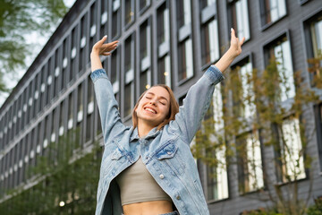 Satisfied young woman with long loose hair widely smiles raising arms upward. Happy lady stretches...