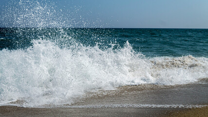 Splashing water drops of sea wave in a sunny day with blue sky.