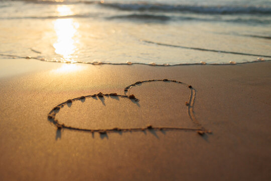 A heart is drawn on the sand on the beach at sunset. Romantic sunset on the beach. Heart shape. Heart symbol.