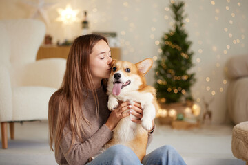 a brunette girl holds and hugs a red corgi dog on a clean light background, the concept of love for animals, selective focus