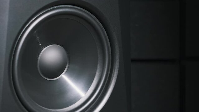Studio monitor speaker vibrates from bass music in a recording studio, close-up. Modern loudspeaker membrane moves while listening loud song in slow motion. Working bass speaker on low frequency. HiFi
