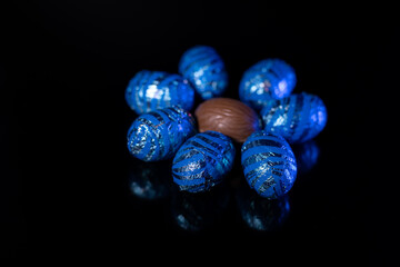 Chocolate eggs with and without paper. Black background. Easter eggs.