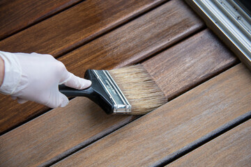 Wooden flooring oil treatment, hand with a brush applying transparent wood protector close up