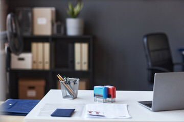 Workplace of white collar worker with laptop, stamps for documents and other supplies on desk standing in front of camera in coworking space