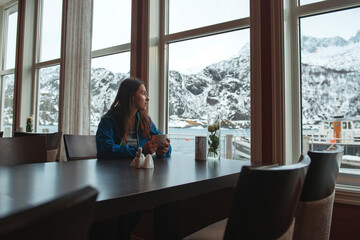 Lofoten islands, Senja region, Norway. Winter. Young brunette girl sitting in cafe with Cup of...