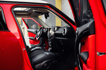 Compact, stylish and youthful crossover in bright red color. Modern black car interior.  Details...