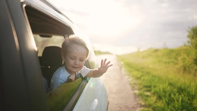 free boy kid hand from the window rides in a car wind in the face. conceptual journey of a car on the road. The boy son stretches out his hand from the car window, the sun lifestyle glare of sunset