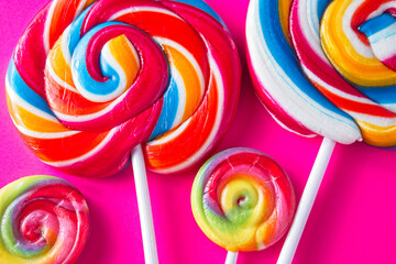 Big and small stripy candy lollipops on a bright pink background