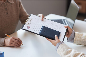 Hands of young female applicant passing filled form to manager of visa application center for consideration and stamping