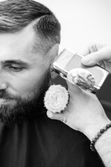 Barber shaves the temple with cordless trimmer during a short haircut on the sides of the head.