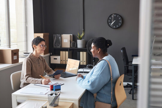 Young African American female applicant answering questions of manager working in visa application center during conversation in office