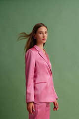  Fashionable beautiful confident woman wearing trendy pink satin suit blazer, trousers, posing on green background. Studio fashion portrait - 678879014
