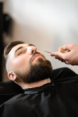 A barber stylist trims a Caucasian mans mustache with scissors