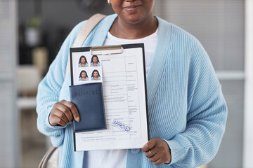 Cropped shot of young African American woman in blue cardigan showing filled visa application form...