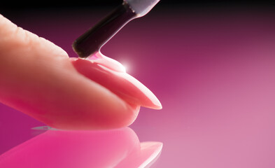 Applying Nail polish, pink shellac UV gel, varnish, manicure process concept in beauty salon. Transparent top coat drop on brush. Over pink background. Application of nail polish - obrazy, fototapety, plakaty