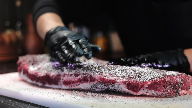Male chef hands adding seasonings herbs salt cooking farm meat steak on marble board at restaurant