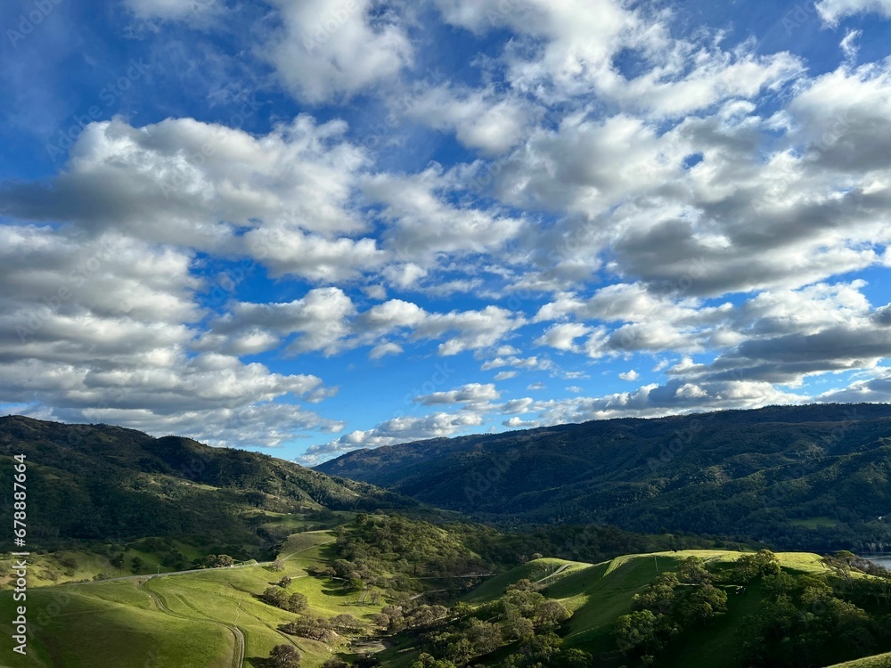 Sticker Gorgeous view of a green valley with a vast forest under a sunny sky covered with clouds