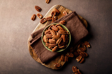 Pecan nuts in a bowl on a brown background, top view