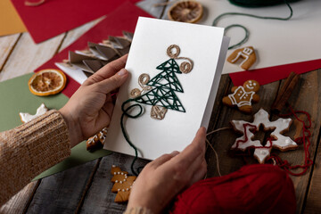 Woman creating handmade craft paper christmas card with wool thread fir tree. Idea for quality family time with children, do it yourself present, hobby, holiday leisure activity. Recyclable materials