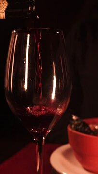 Vertical closeup of the red wine being poured into a glass.
