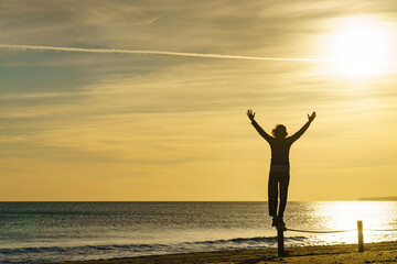 Woman on beach enjoy sunrise with arms up