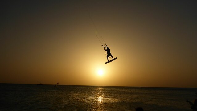 Silhouette of a person kitesurfing in the sea with the bright golden sunset in the background