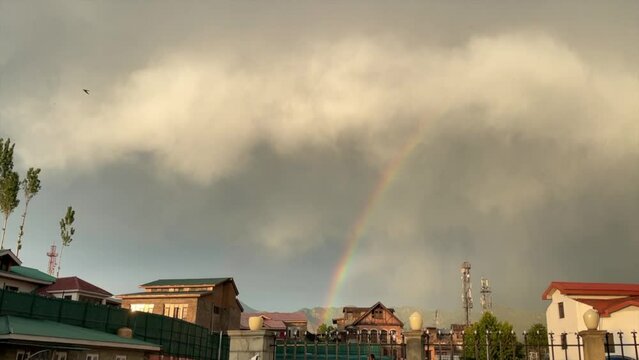 Low angle footage of a rainbow in the air before the gloomy clouds in the city of Srinagar