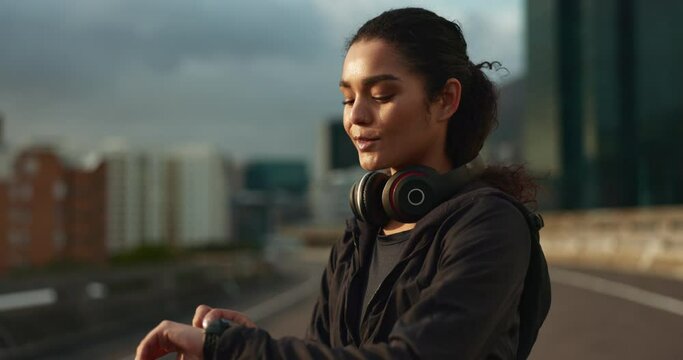 Headphones, watch and woman athlete in the city for race, marathon or competition training. Breathe, sports and young female runner listen to music on break for running cardio workout in town.