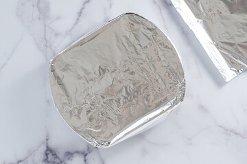 Baking dish covered with aluminum foil close-up on a marble kitchen table, flat lay