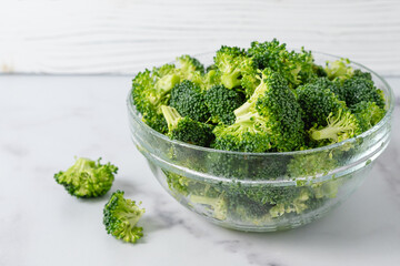 Glass bowl of fresh raw organic broccoli close-up on a marble kitchen table in a light background