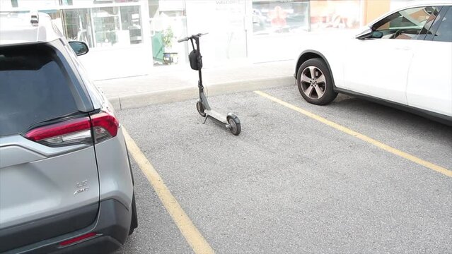 electric scooter taking up entire whole parking spot space in between two cars vehicles in front of store storefront and sidewalk