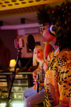 Profile of a multiracial vocalist singing to a microphone at a recording session in a studio.