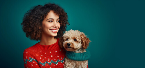 Smiling young girl with wild curly afro hairstyle, standing in front of a blue paper background with a cute dog, wearing a comfortable warm sweater with New Year's motifs.