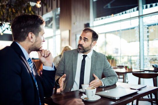 Mature businessman mentoring younger colleague in cafe meeting