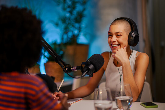 Portrait of a happy journalist sitting in a home broadcasting studio and interviewing a guest in her podcast.