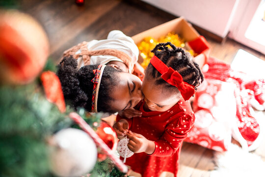 Little girl kissing sister on cheek and decorating Christmas tree - Powered by Adobe