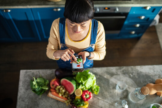 Top view of woman taking picture of different vegetables and fruits on kitchen countertop