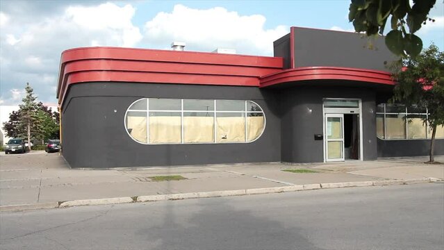 empty vacant restaurant store storefront with windows covered from inside and front entrance door open with leaves branch blowing in front, red and gray