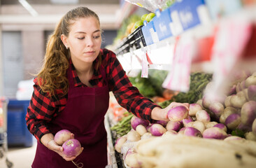 Young woman seller lay out ripe purple turnip on the counter at vegetable shop
