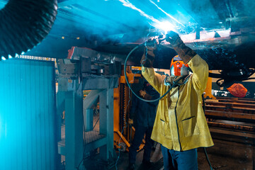 man working under a train using a welder  - obrazy, fototapety, plakaty
