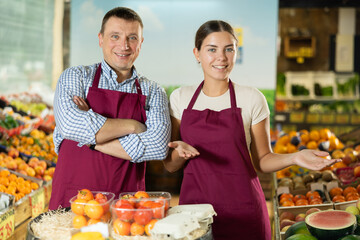 Friendly man owner of fruit-vegetable shop standing in trading floor with girl assistant....
